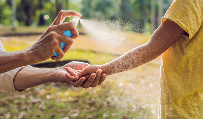 Photo of a young person's arm being sprayed with insect repellent